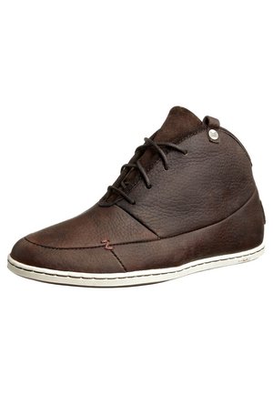 Chaussure montante à la cheville en cuir marron avec lacets noirs, semelle blanche et surface texturée, avec une petite étiquette logo métallique près du col.