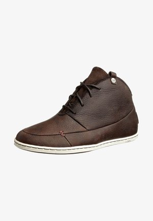Chaussure montante à la cheville en cuir marron avec lacets noirs, semelle blanche et surface texturée, avec une petite étiquette logo métallique près du col.