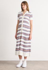 Φόρεμα με γιακά μέχρι το γόνατο σε ριγέ σχέδιο σε μπλε, πορτοκαλί και λευκό, με κοντά μανίκια και κουμπιά μπροστά, συνδυασμένο με λευκά αθλητικά παπούτσια.