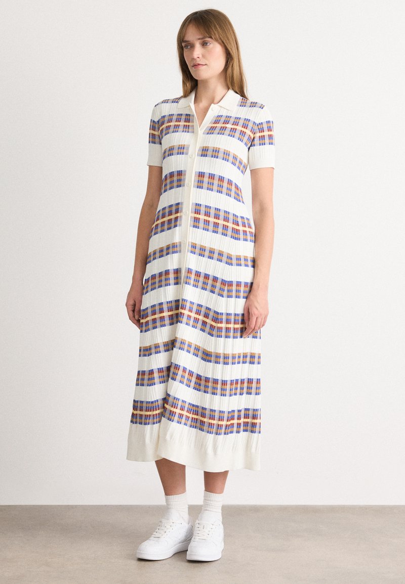 Φόρεμα με γιακά μέχρι το γόνατο σε ριγέ σχέδιο σε μπλε, πορτοκαλί και λευκό, με κοντά μανίκια και κουμπιά μπροστά, συνδυασμένο με �λευκά αθλητικά παπούτσια.