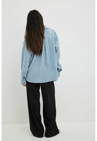 Light blue, oversized shirt with long sleeves, button cuffs, and a straight hem, paired with black, wide-leg trousers. Smooth fabric texture.