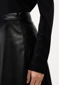 Sort lædernederdel med en glat tekstur, der har en sidelukning og en tætsiddende talje. Stoffet har en let skinnende overflade og en struktureret form.