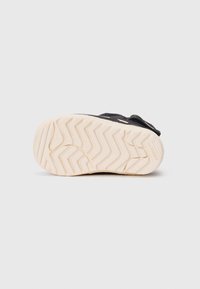 Basket noire avec semelle à motif zigzag blanc, face vers le haut sur un fond blanc uni, logo Adidas visible sur le bord de la semelle.