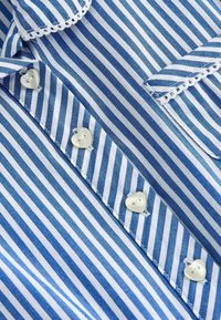 Tissu en coton rayé bleu et blanc avec des boutons en forme de cœur. Dispose d'un col festonné et de bords soigneusement cousus.