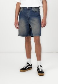 Blå denimshorts med en falmet finish, der har et fem-lommers design, standard talje og en lige pasform til knæet, parret med sorte sneakers.