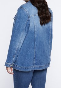 Džínová bunda v medově modré barvě, s uvolněným střihem, knoflíkovými manžetami a viditelnými švy, s lehce vybledlým vzhledem.