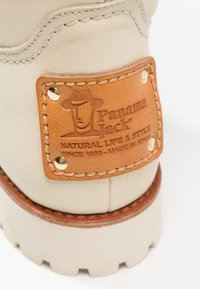 Talons de bottes en cuir beige avec une étiquette en cuir marron cousue embossée de "Panama Jack Natural Life & Style Depuis 1989 Fabriqué en Espagne."