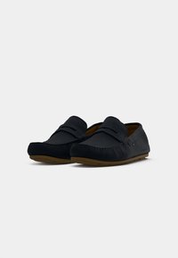 Sorte ruskind loafers med syet detaljer, flade gummisåler og en glat overflade. Designet har en let hæl og minimale detaljer.