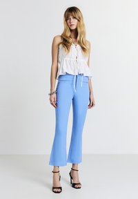 Pantaloni a palazzo azzurro chiaro realizzati in tessuto morbido, con vita alta e tasche laterali, abbinati a una maglietta senza maniche bianca. Sandali neri con tacco.