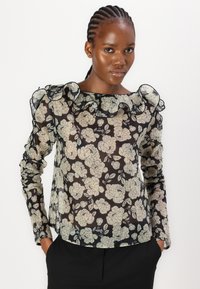 Transparante zwarte blouse met witte bloemenprint, geplooide mouwen en een ruches halslijn. Beschikt over een ontspannen pasvorm en een lichte textuur.