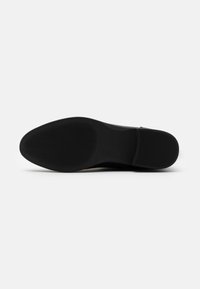 Black shoe sole with a textured, wavy pattern. Rounded toe and smooth edges. Made of rubber, minimalistic design with no visible logos.