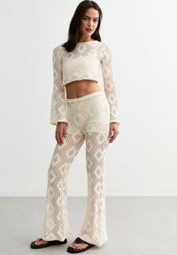 Vit, långärmad cropped topp och vida byxor i öppenstickad virkning med geometriska mönster. Outfiten har en texturerad, lätt design.