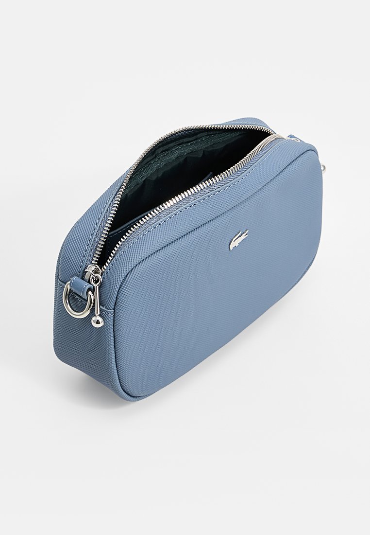 Trousse de maquillage en tissu texturé bleu avec une fermeture éclair argentée, arborant un logo sur le devant et une doublure intérieure verte.