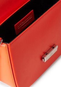 Borsa a mano rossa in pelle con forma strutturata, chiusura in metallo argento e interno nero a texture, con uno scomparto per carte firmato.