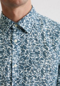 Chemise à manches courtes en tissu léger, dotée d'un motif abstrait de galets bleus et blancs, avec un col à rabat et des boutons sur le devant.