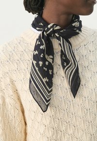 Marineblå silkeslør med blomster- og stribemønstre, bundet om halsen, bærer over en struktureret cremet strikket trøje. Knudret stil, letvægtsstof.