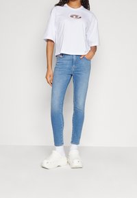 Camiseta corta blanca con un detalle recortado, combinada con jeans ajustados azul claro y zuecos blancos. Tejido suave y corte ajustado.