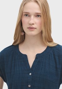 Dunkelblaue Bluse mit kurzen Ärmeln und rundem Halsausschnitt aus strukturiertem Stoff, mit kleinen Knöpfen auf der Vorderseite. Mit Raffung ausgestattet.