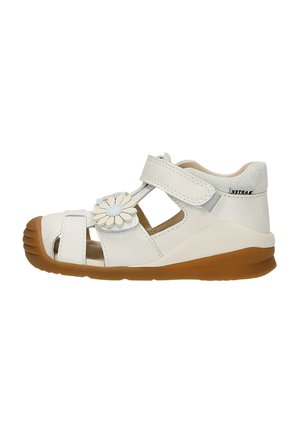 Sandalo bianco per bambino con suola di gomma marrone, cinturino regolabile in velcro, punta aperta e fiore decorativo sulla parte superiore.