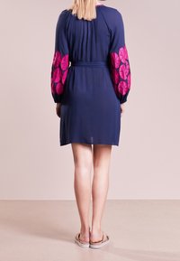 Marinblå klänning med rosa mönstrade puffärmar, åtsittande midja och en flödande silhuett, med en slät textur och knälång längd.