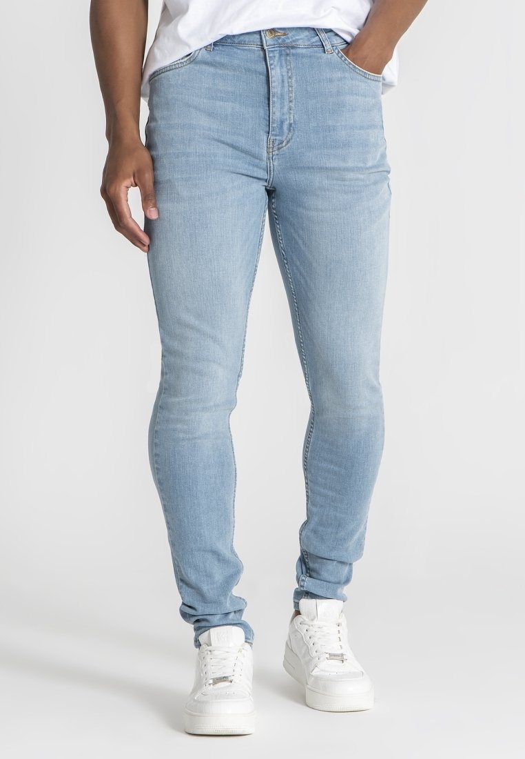 Světle modré slim-fit džíny vyrobené z denimu, s hladkou texturou, pětikačkovým designem a jemně vybledlými detaily, doplněné bílými teniskami.