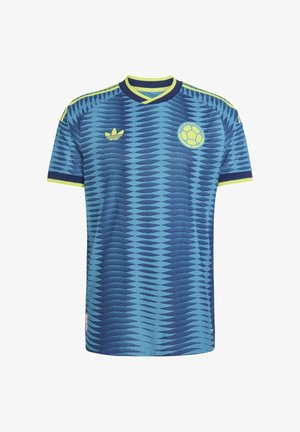 Niebieska koszulka piłkarska z ciemnoniebieskim wzorem fal, żółtym kołnierzem i wykończeniem rękawów, logo Adidas oraz emblematem Kolumbijskiej Federacji Piłkarskiej.