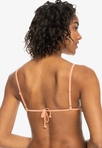 Ferskenfarget bikinitopp med tynne justerbare stropper, båndlukking bak og en jevn tekstur. Minimalistisk design med en klassisk silhuett.