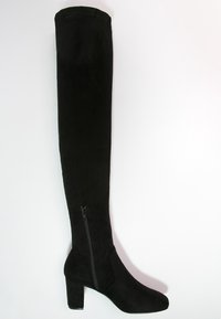 Bota de ante negra, hasta la rodilla, con tacón cuadrado y cremallera en el lado interior. Textura suave y diseño ajustado para una silueta estilizada.