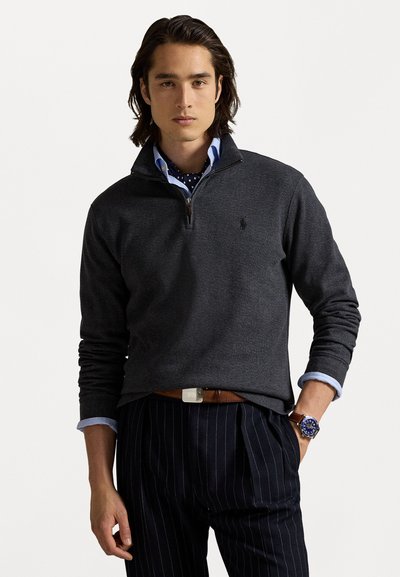 Mørkegrå pullover med kvart lynlås, parret med en lyseblå skjorte og et mønster-scarf, der har smalstribede bukser og et ur.