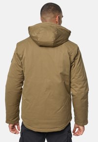 Giacca isolante marrone con cappuccio, caratterizzata da una texture liscia e dettagli cuciti. Il design include un orlo arrotondato e tasche laterali.