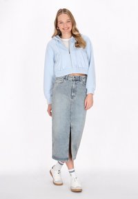 Felpa azzurra corta con lacci, abbinata a una gonna a matita in denim a vita alta con uno spacco frontale. Scarpe da ginnastica bianche e calze.