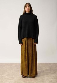Czarny wełniany sweter z golfem o luźnym kroju, zestawiony z długą spódnicą w kolorze musztardowym z kordurowej tkaniny, z pionowymi paskami i miękką fakturą.