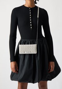 Abito lungo a maniche lunghe nero a coste con scollo rotondo e chiusura a bottoni. Presenta una borsa a tracolla bianca trapuntata con una tracolla a catena.