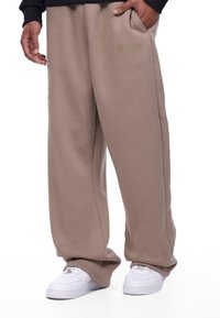 Beige sweatpants made of soft fabric with a loose fit, featuring side pockets and "DROPSIZE" text in a subtle color near the pocket.