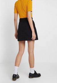 Gonna di jeans nera con taglio dritto, vita alta e dettagli minimi. Abbinata a una maglietta in maglia gialla texturizzata e scarpe con lacci nere.