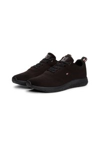 Paire de baskets noires avec texture tricotée, lacets noirs, et petit logo rouge, blanc et bleu sur le côté et la languette arrière.