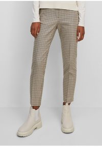 Pantalon à carreaux beige et marron de coupe slim, associé à des bottines beiges claires avec une semelle épaisse et des panneaux élastiques sur les côtés.