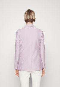 Dopasowana blazerka w kolorze lawendowym z wyciętym kołnierzem, długimi rękawami i dopasowanym krojem. Teksturowana tkanina, pojedynczy rozporek z tyłu, akcenty guzikowe.