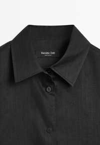 Camicia nera con colletto classico, chiusura a bottoni e tessuto a trama. Presenta un'etichetta con "Massimo Dutti" all'interno del colletto.