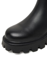 Must mustad nahkasaapad ümara varbaga ja paksu musta kummitaldaga, millel on selgelt väljendatud mustrit ja tekstureeritud serv.