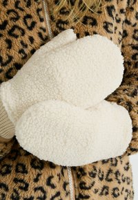 Des moufles couleur crème en polaire douce et texturée, avec une forme arrondie et des poignets en tricot, associées à une veste à motif léopard.