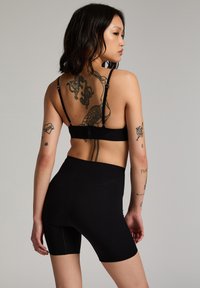 Soutien-gorge de sport en tissu noir avec bretelles réglables, associé à un short de vélo noir taille haute. Les deux vêtements ont une texture lisse.