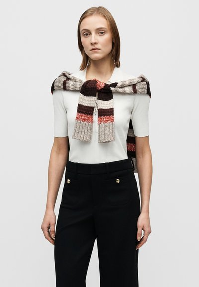 Sciarpa lavorata a maglia con motivo a strisce in marrone, rosso e beige drappeggiata su una maglietta aderente bianca; abbinata a pantaloni neri su misura con dettagli dorati.