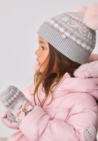 Graue gestrickte Mütze mit hellrosa Bommel und Mustern, kombiniert mit grauen Fäustlingen mit rosa Schleife und goldenen Details, getragen zu einer rosa Steppjacke.