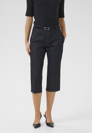 Tumman denim-kankaan cropped-housut, joissa on kapea leikkaus, etutaskut ja musta vyö. Yhdistetty mustiin korkokenkiin.