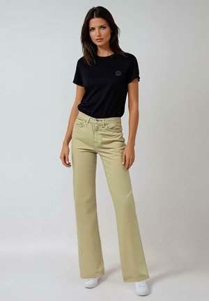 Zwart katoenen T-shirt met opgerolde mouwen en ronde halslijn, gecombineerd met licht kaki flare-broek en witte sneakers. Eenvoudig en casual ontwerp.