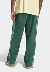 Green athletic pants with two side stripes in light gray, made of soft material, featuring a relaxed fit and elastic waistband.
