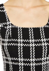 Schwarz-weiß gemusterte Bluse mit quadratischem Ausschnitt, im Karodesign und mit durchgehend gerippter Textur.