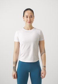 Világos rózsaszín, testhez simuló, rövid ujjú póló puha pamutból, turkiz leggings-szel párosítva. Minimalista dizájn, sima textúra és egyszerű nyakvonala van.