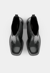 Black leather Chelsea boots with a sleek, glossy finish, rounded toe, and elastic side panels. Minimalist design with a subtle logo detail.